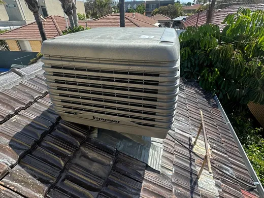Roof-mounted evaporative air conditioning unit on a tiled roof against a blue sky