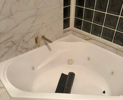 Corner spa bath with a dark tiled feature splashback