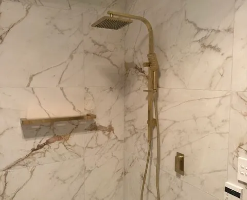Marble-look shower wall with a brushed brass handheld shower fixture