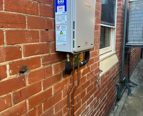 Continuous-flow gas hot water unit installed on a red brick wall
