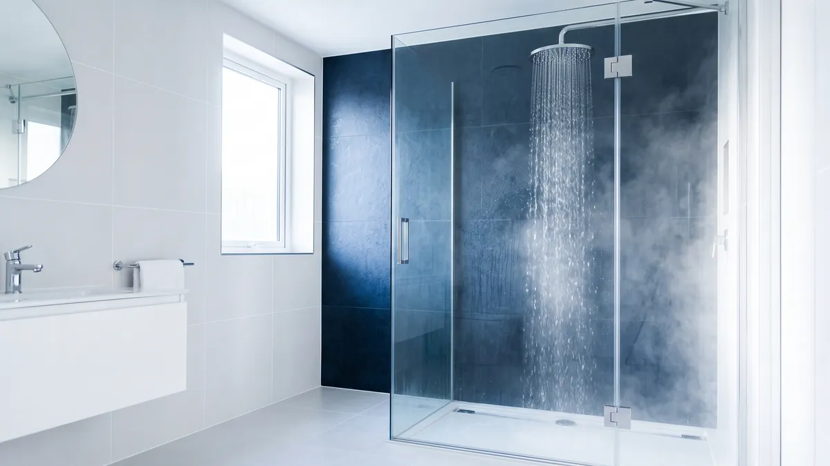 Steaming hot water running from a chrome rainfall shower head in a clean white and navy tiled bathroom