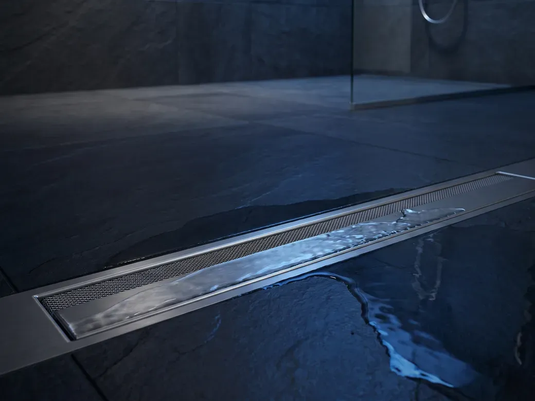 Water draining cleanly through a sleek stainless linear floor drain in a modern wet room