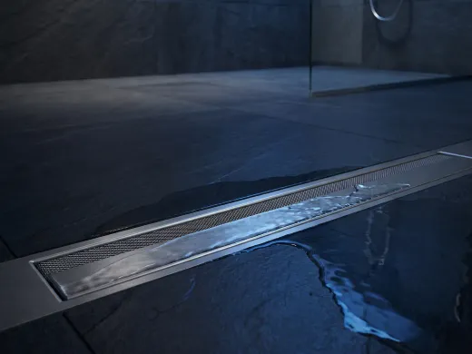 Water draining cleanly through a sleek stainless linear floor drain in a modern wet room