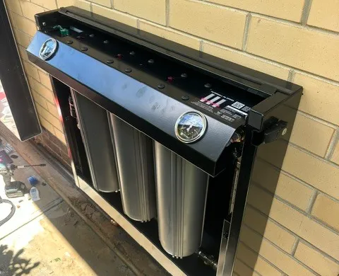 Multi-stage whole-home water filtration system installed against an exterior wall